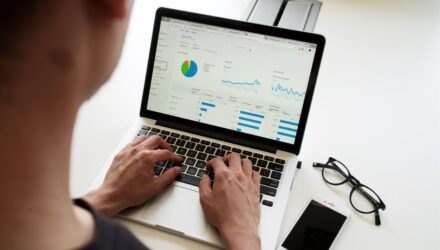Photo taken over a man's shoulder, as he is working on a Macbook, looking at a series of charts and graphs.