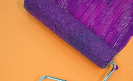 A paint roller applying a deep purple stripe to a vibrant orange wall.